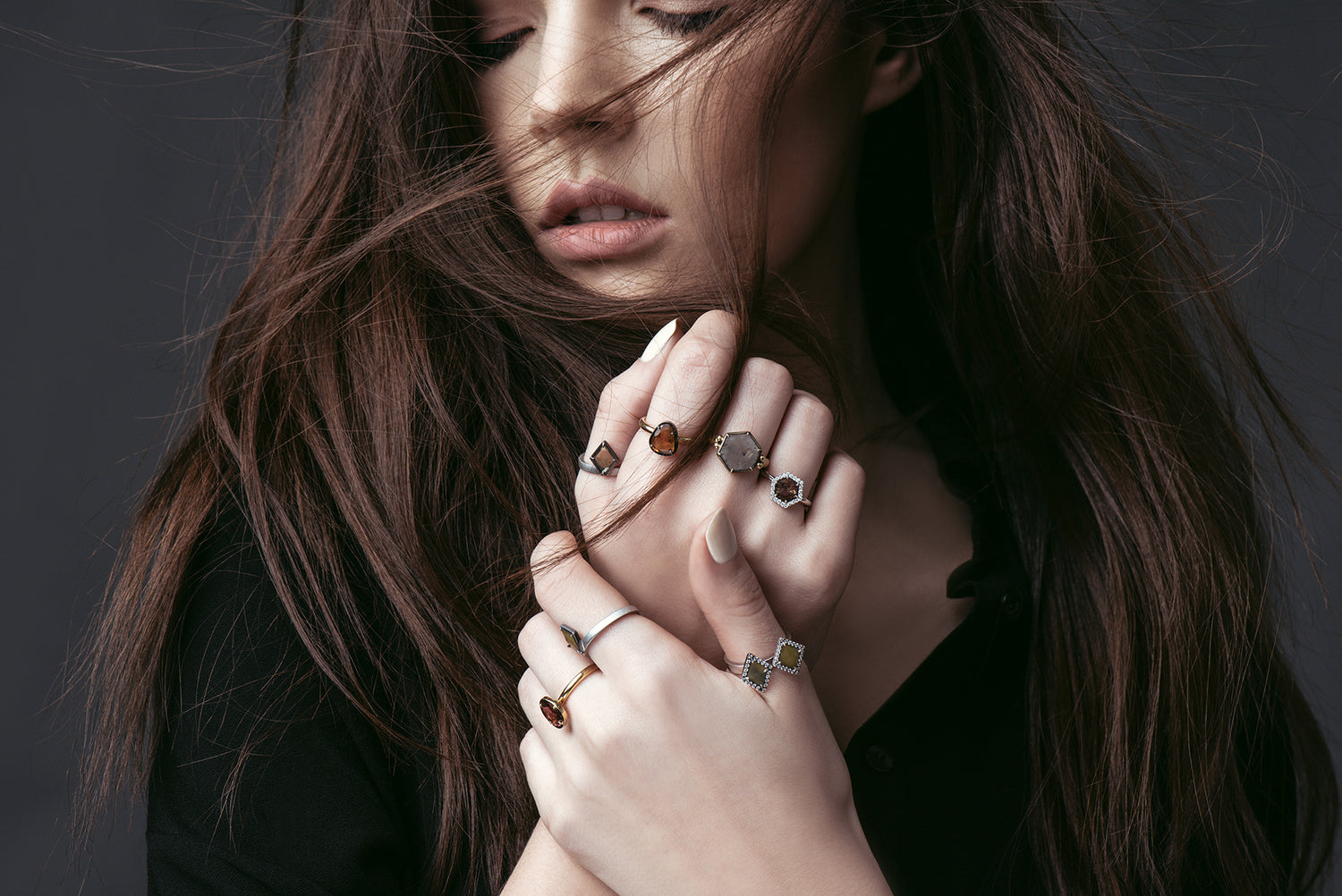 Woman wearing multiple 18K rings on a dark background